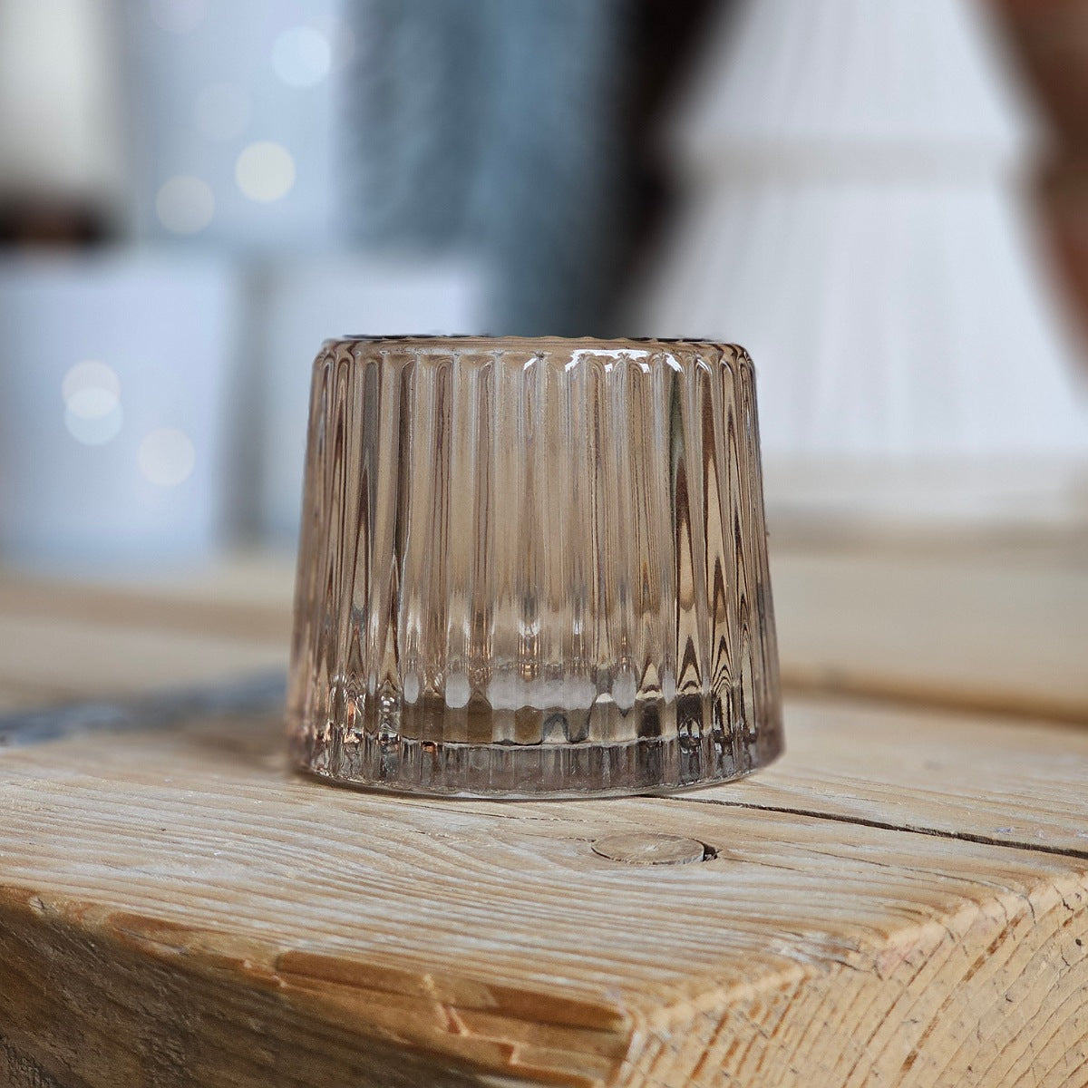 Smoky glass candle holder on a wooden surface with a blurred background