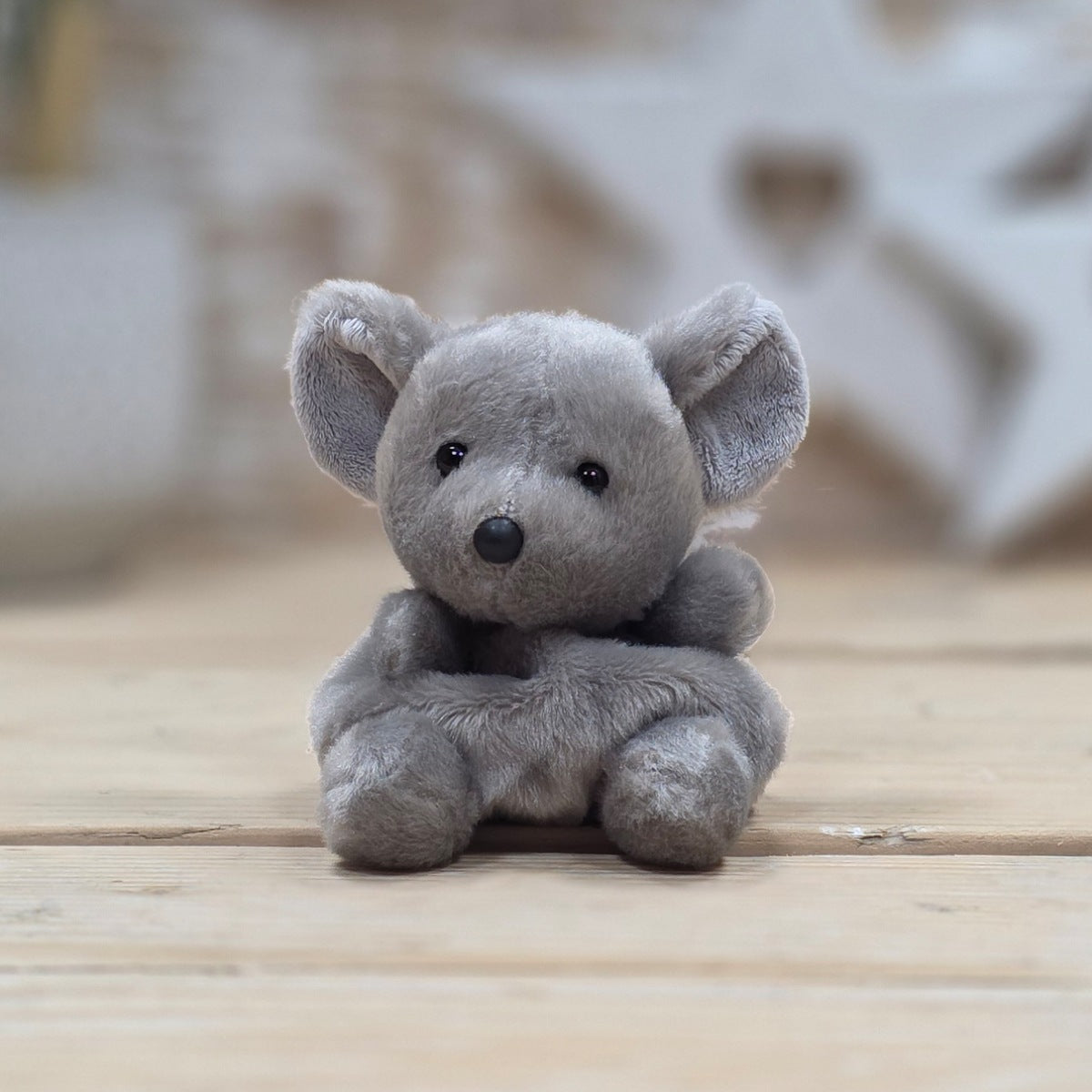 Gray stuffed animal sitting on a wooden surface with a blurred background