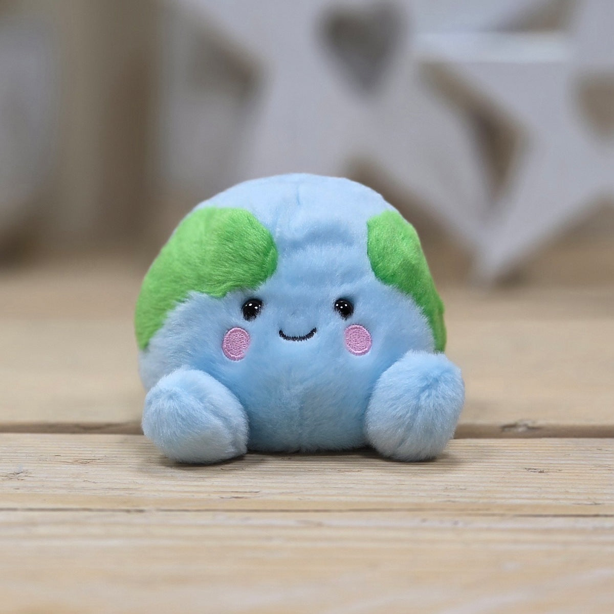 A small plush toy shaped like a cute blue globe with green continents, pink cheeks, and a smiling face, sitting on a light wooden surface.