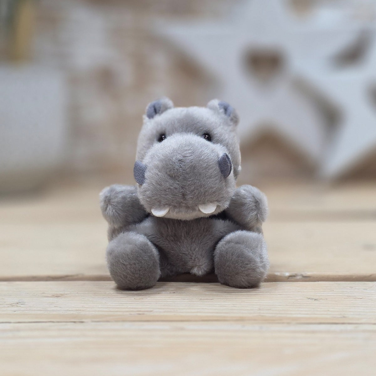 A small gray hippo plush toy sitting on a light wooden surface with a softly blurred indoor background.