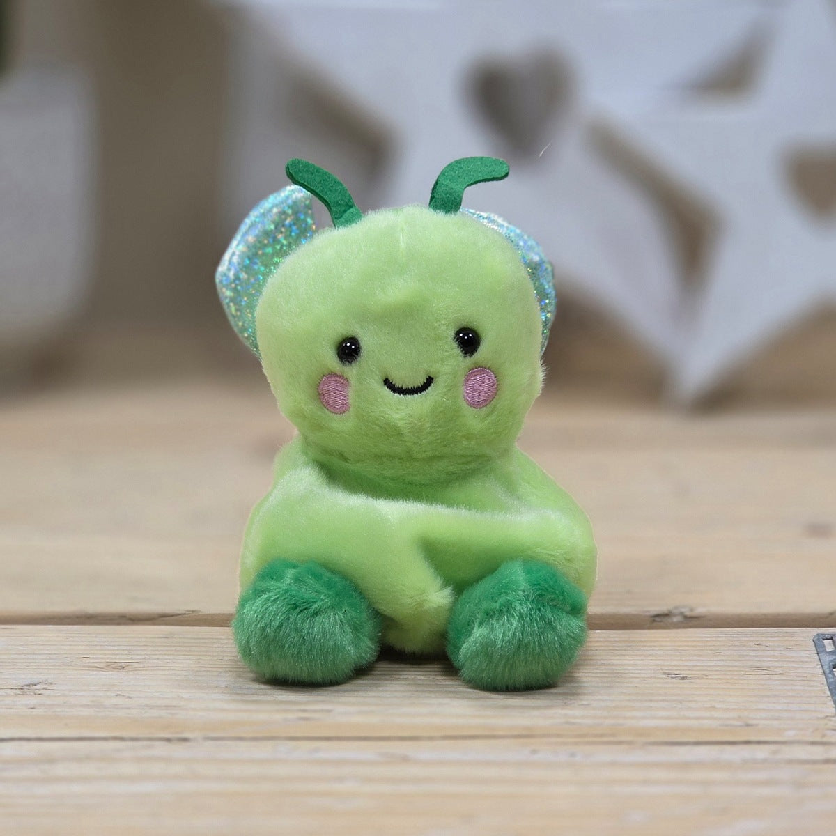 Green plush toy with a smiling face on a wooden surface