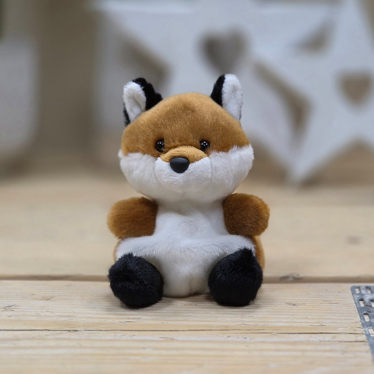 Plush toy fox sitting on a wooden surface with a blurred star-shaped object in the background