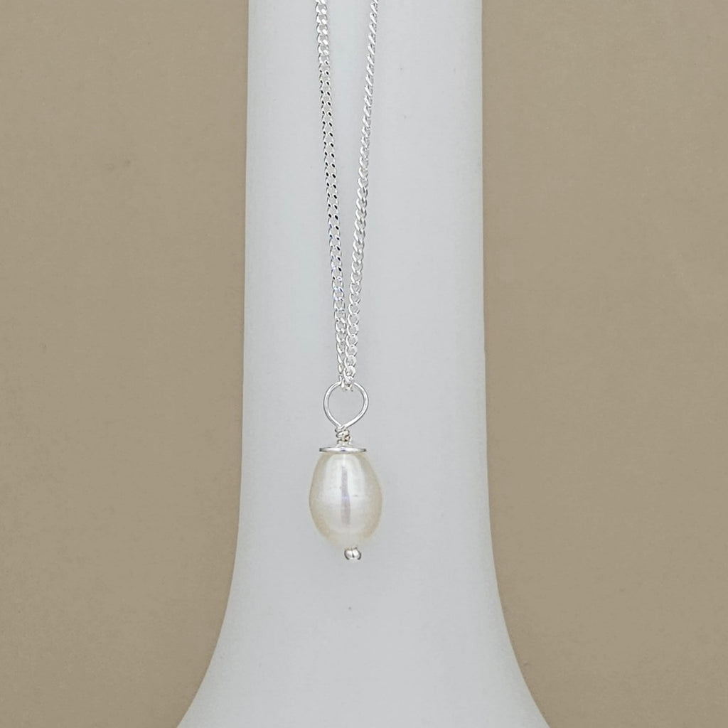 A silver chain necklace with a single teardrop-shaped white pearl pendant, displayed on a white jewelry bust against a beige background.