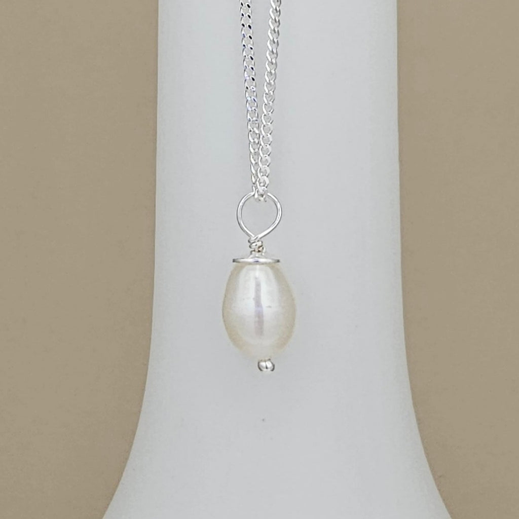 A silver chain necklace with a teardrop-shaped white freshwater pearl pendant, displayed on a white jewelry bust against a beige background.