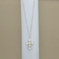 A silver chain necklace with a cross-shaped pendant made of white faux pearls, displayed on a white cylindrical stand against a beige background.