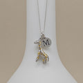 Necklace with a silver and gold giraffe pendant and silver disc featuring a letter 'M' on a white stand.