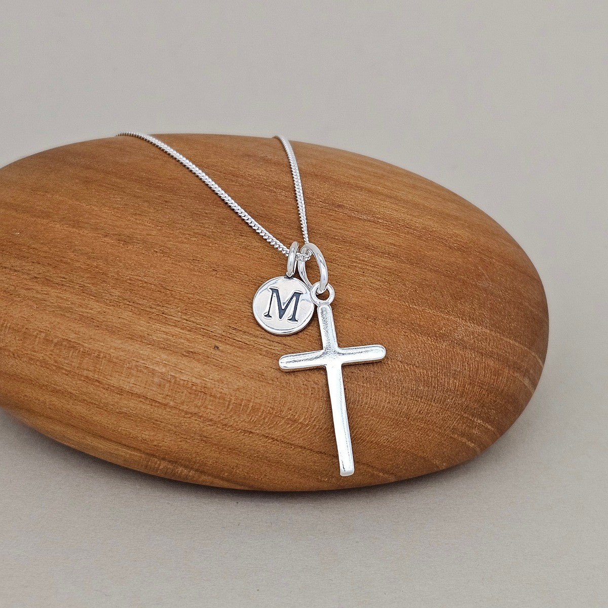 Silver cross necklace with a round pendant on a wooden rock