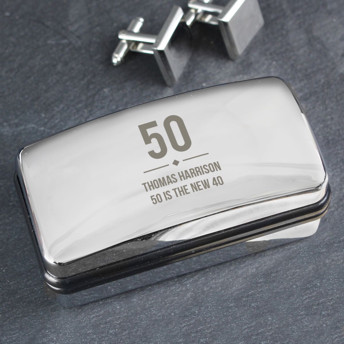 Silver cufflink box with engraved text on a dark surface