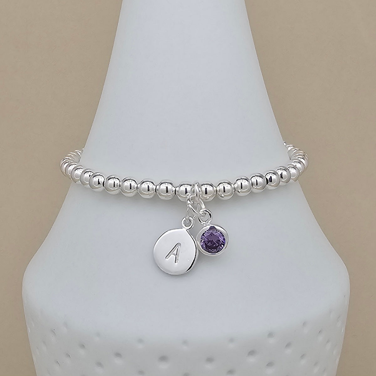Silver beaded bracelet with a purple charm and engraved disc on a white bust