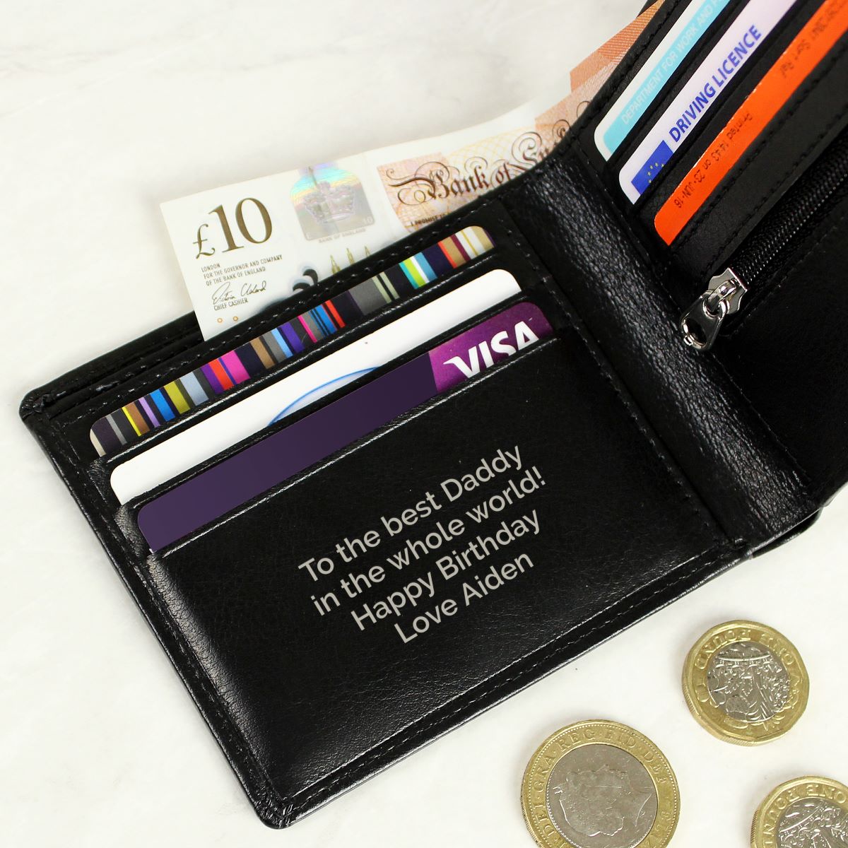 Black wallet with engraved message, cards, and coins on a white background
