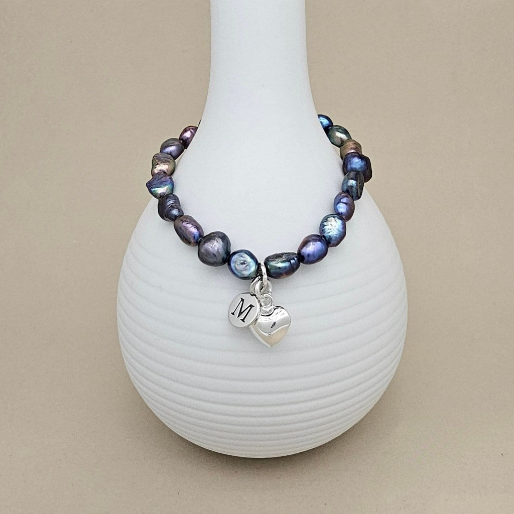 Pearl bracelet with a heart charm on a white vase against a beige background
