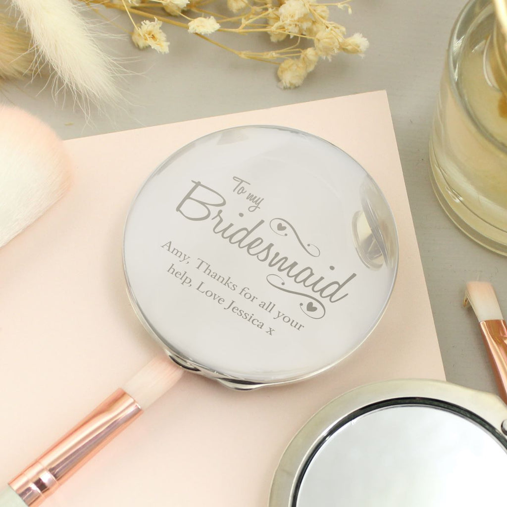 Personalized compact mirror with engraved message on a light surface with decorative elements.