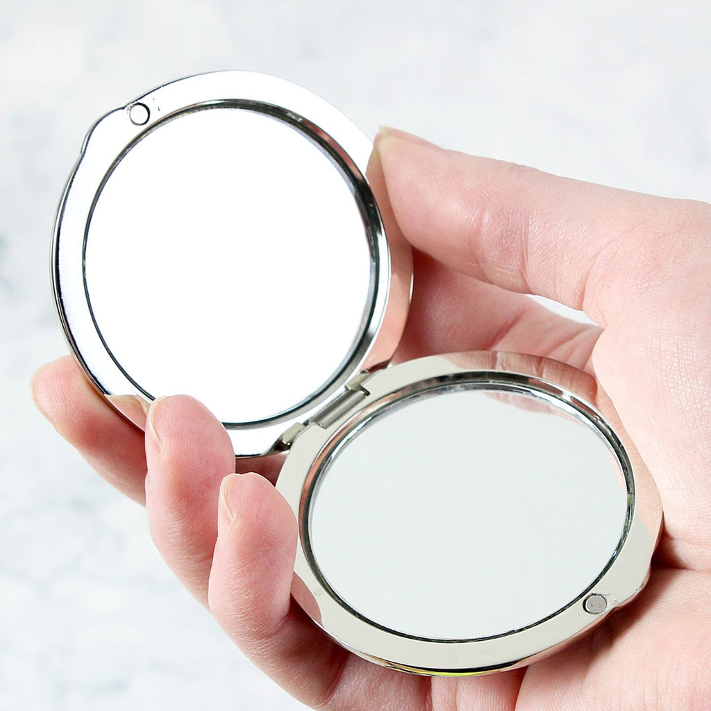Compact mirror held in a hand against a light background