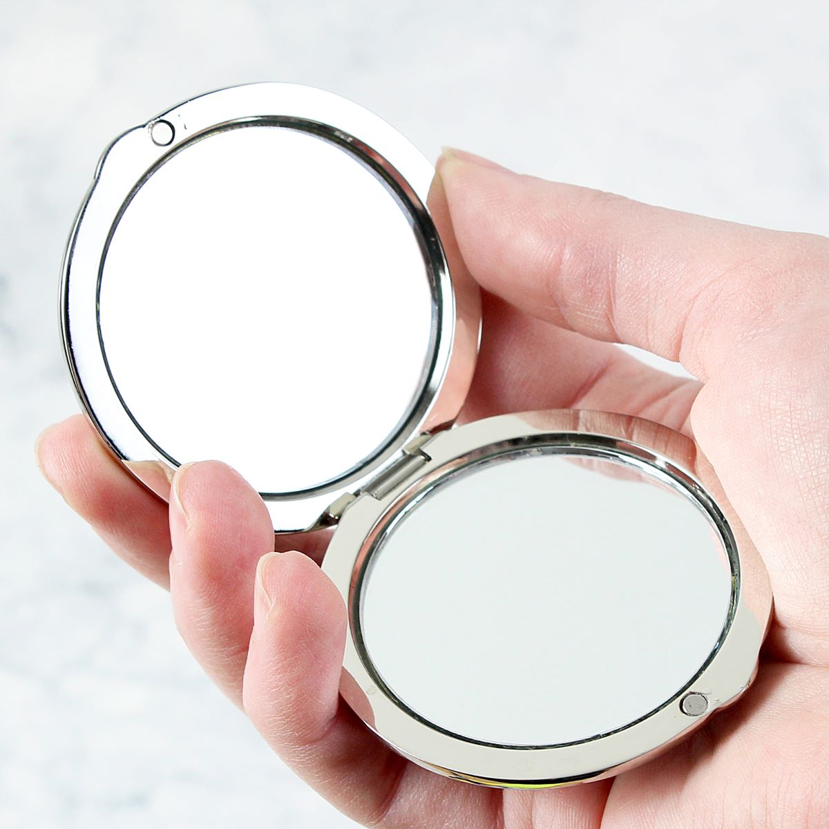 Compact mirror held in a hand against a light background