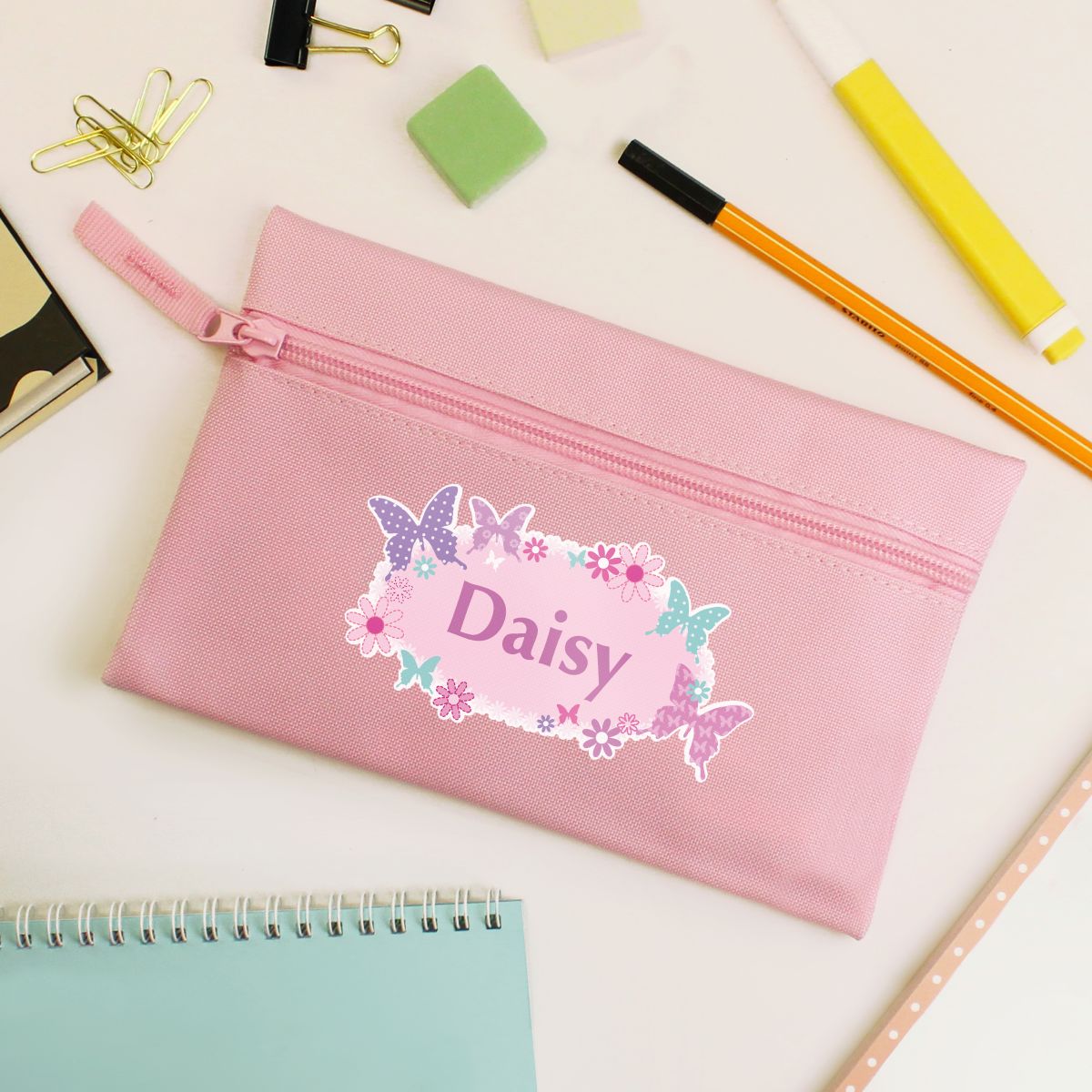 Pink pencil case with the name 'Daisy' with a butterfly design on a desk with stationery items