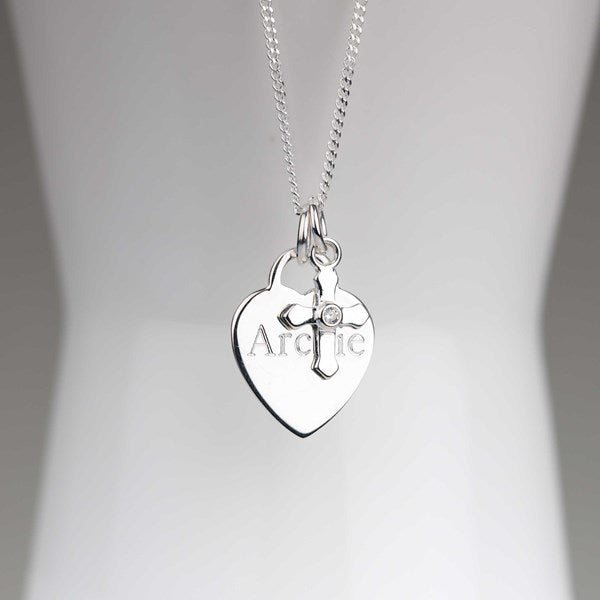 A silver heart-shaped pendant necklace with a small cross charm and a clear rhinestone, displayed on a white mannequin torso. The pendant is engraved with the word 'Archie'.