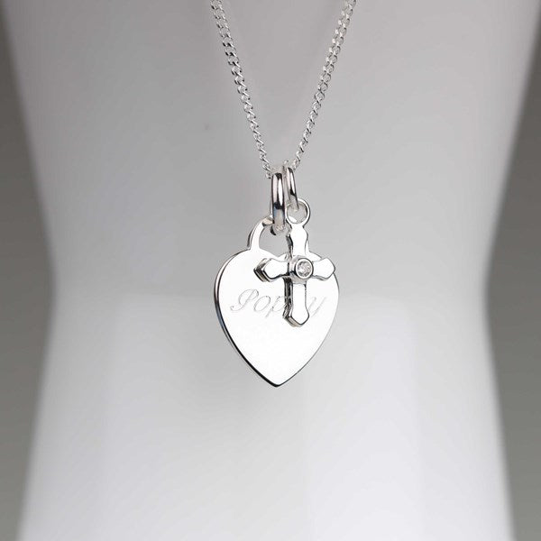 A silver heart-shaped pendant necklace with a small cross charm and a clear rhinestone, displayed on a white mannequin bust.