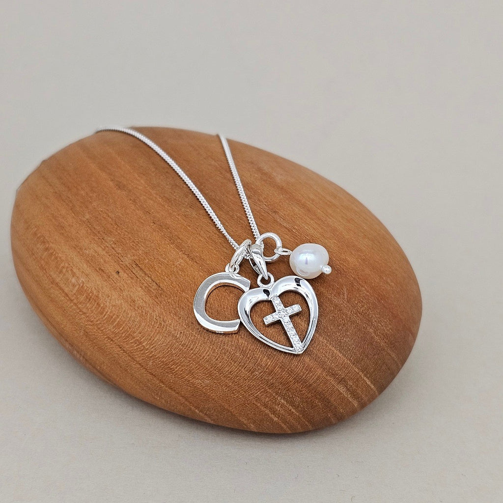 Silver necklace with heart and cross pendant on a wooden rock