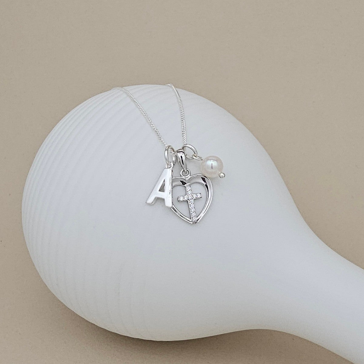 Silver necklace with heart charm, letter 'A', and cross on a beige background