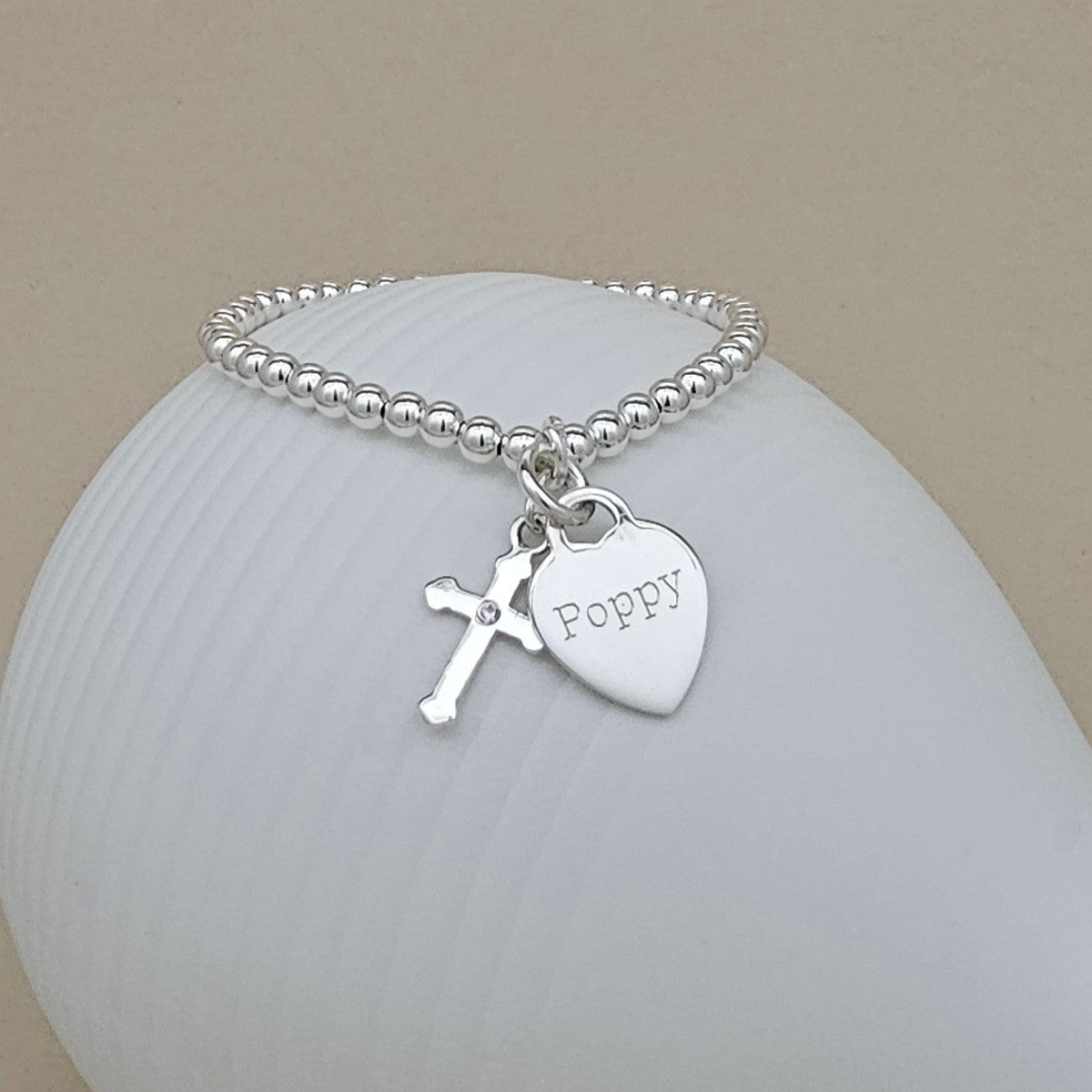 Silver bracelet with a heart charm and cross pendant on a white stone background
