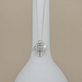 Silver necklace with a cross and heart pendant on a white stand against a beige background