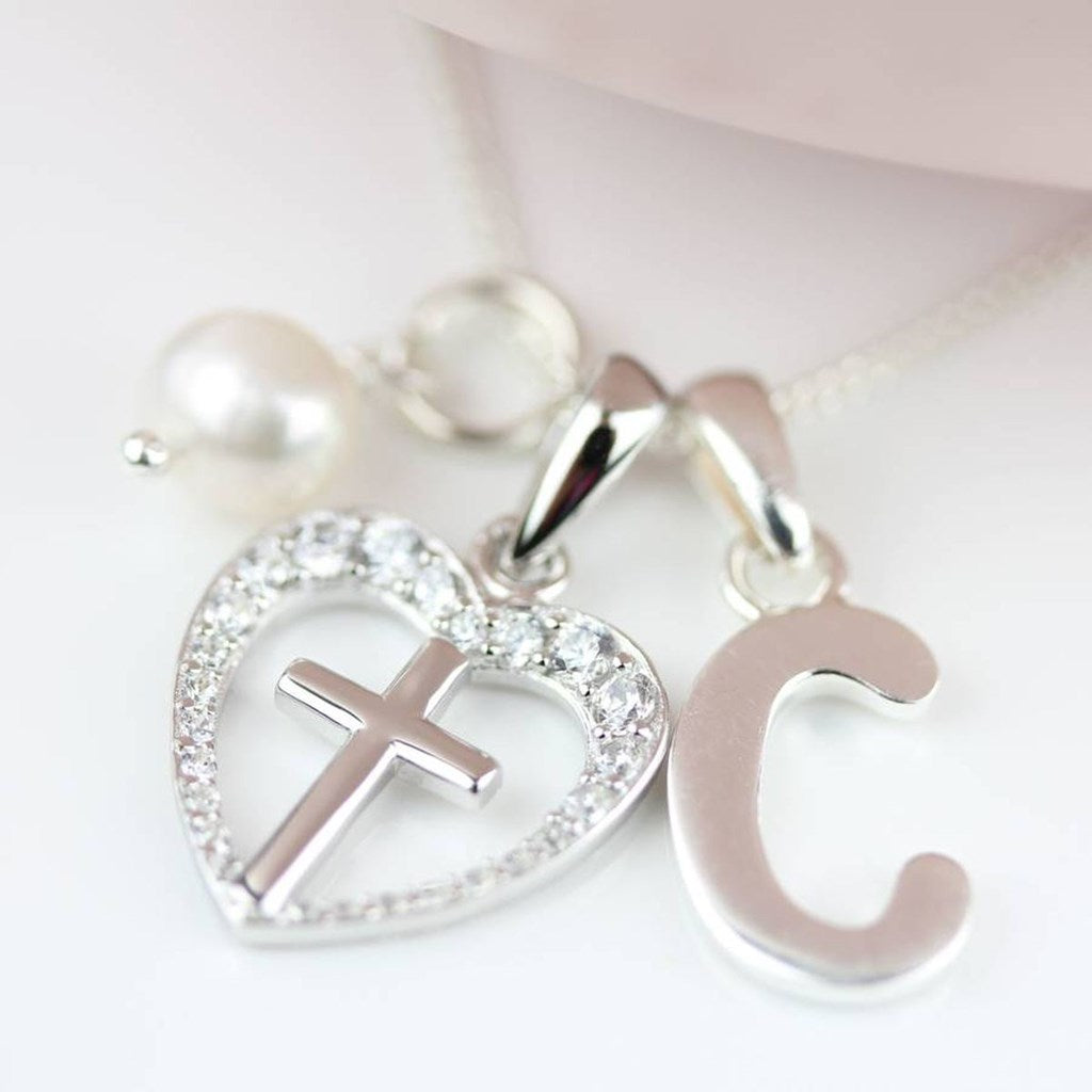 Silver necklace with heart pendant, cross, and letter 'C' on a white background