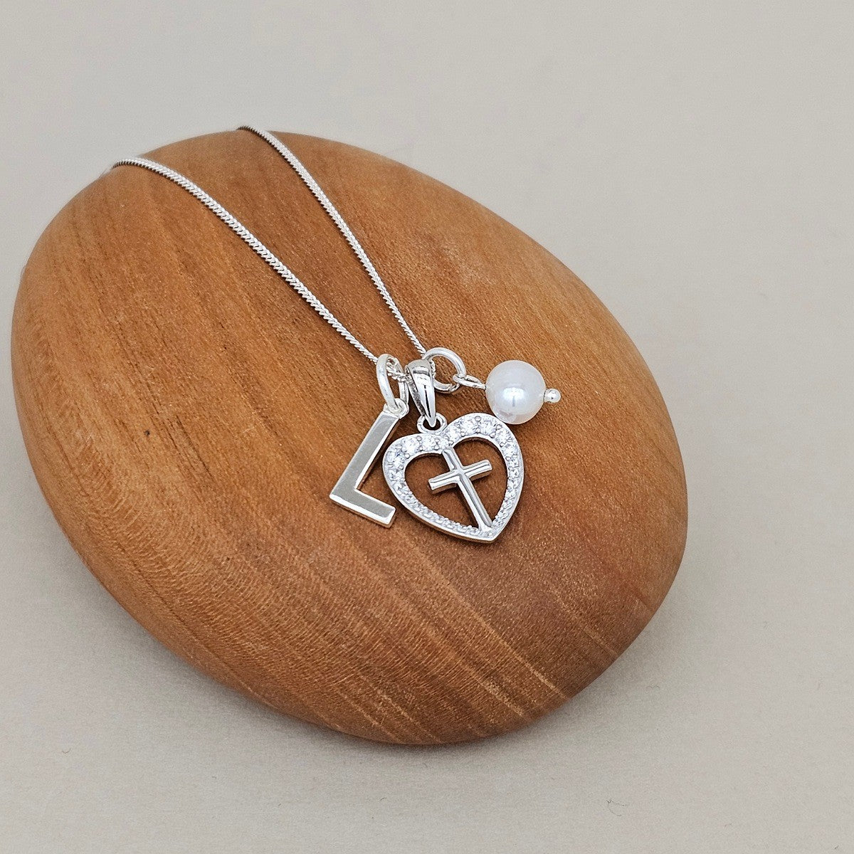 Silver necklace with heart and cross pendant on a wooden rock