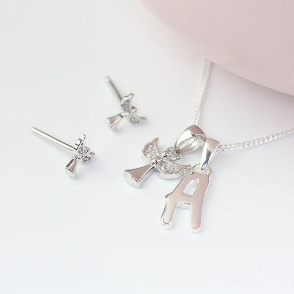 Silver jewelry set featuring a necklace with a winged angel pendant and an initial letter 'A' charm, alongside matching stud earrings, displayed on a clean white surface with a soft pink background element.