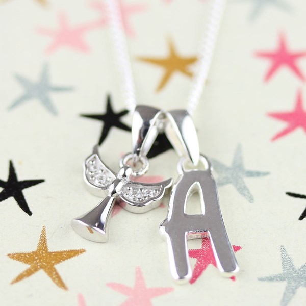 A silver initial pendant necklace featuring the letter 'A' and a small angel wing charm, both adorned with clear rhinestones, hanging from a white chain against a light background with colorful star confetti.