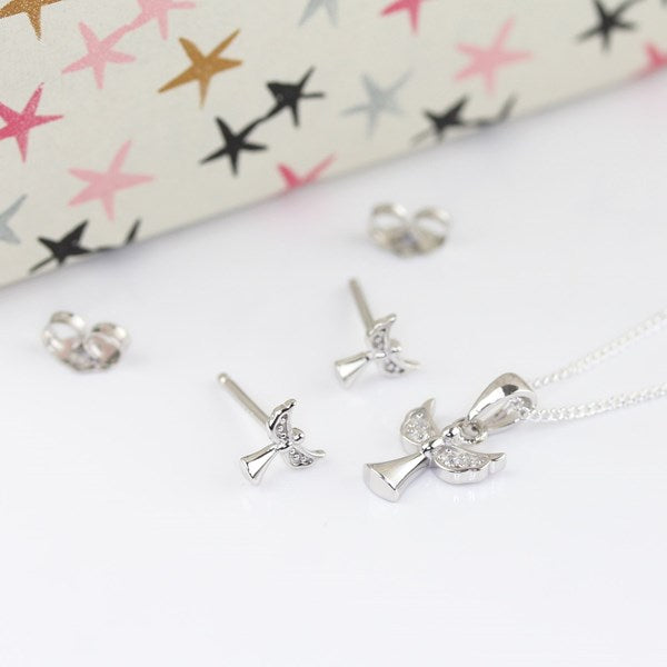 Silver angel jewelry set including a pendant necklace, stud earrings, and a heart-shaped charm, displayed on a white surface with a patterned gift box in the background.