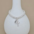 Silver beaded bracelet with a letter 'E' charm and cross pendant on a white vase.