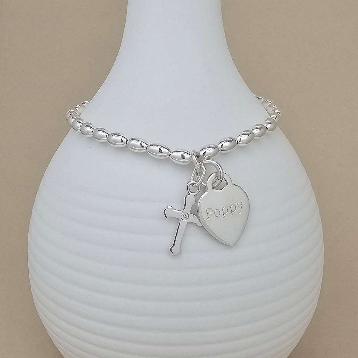 Silver bracelet with a heart-shaped charm engraved with the name 'Poppy' on a white vase