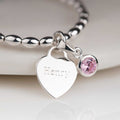 Silver bracelet with a heart-shaped charm engraved 'Henry' and a pink gemstone on a white background