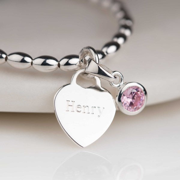 Silver bracelet with a heart-shaped charm engraved 'Henry' and a pink gemstone on a white background