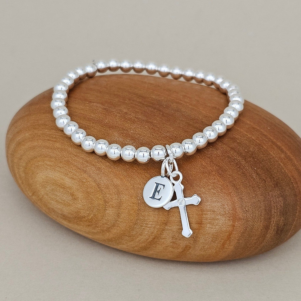 Silver bracelet with a silver cross and 'E' charm on a wooden rock