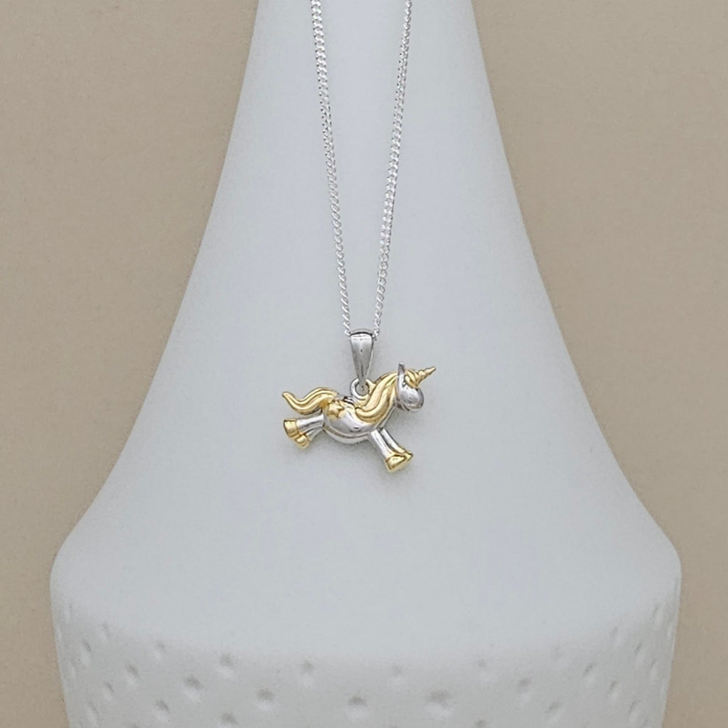 A two-tone silver and gold unicorn pendant necklace displayed on a white textured cone stand against a neutral beige background.