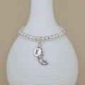 Silver bracelet with a moon charm and letter 'E' on a white vase.