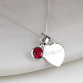 Silver necklace with a heart-shaped pendant with engraved name and red gemstone on a white background