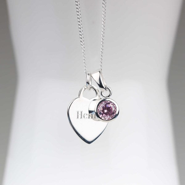 A silver heart-shaped pendant necklace with with engraved name and a small round pink gemstone charm, displayed on a white mannequin bust.