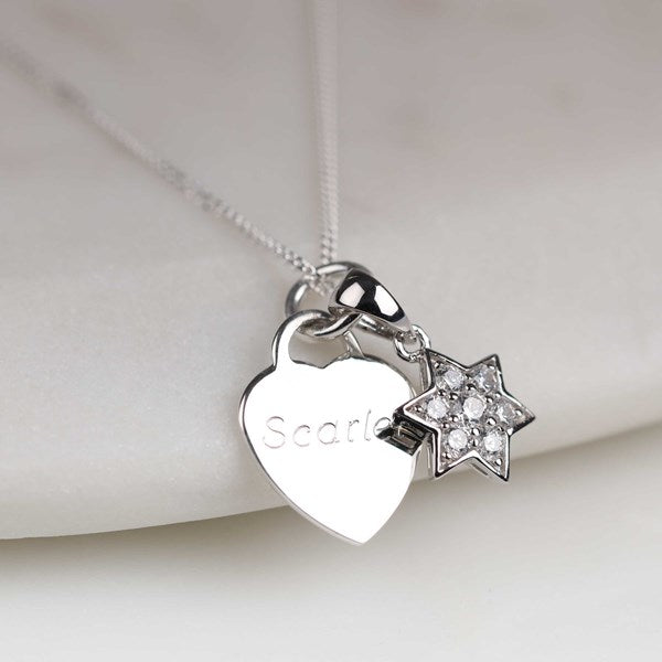 A silver heart-shaped pendant necklace engraved with the name 'Scarlet' and a small star charm set with clear rhinestones, displayed on a soft white fabric background.