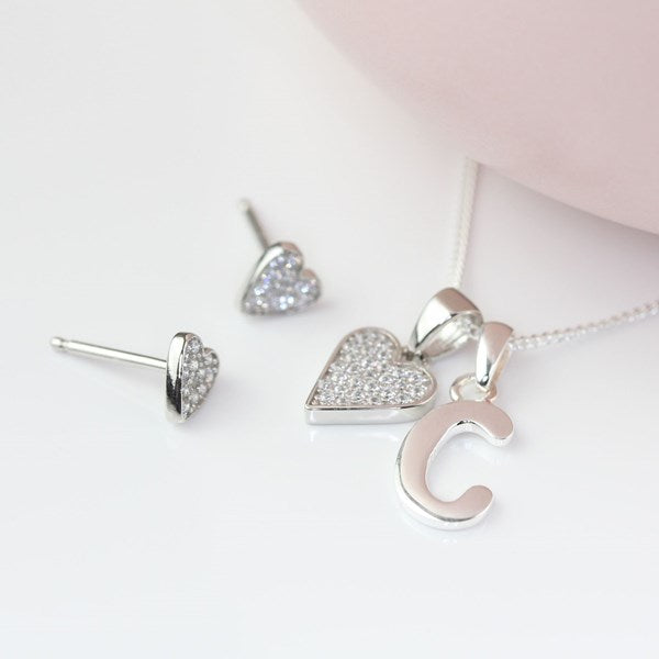 Silver jewelry set with heart-shaped pendant, earrings and letter charm on a white background