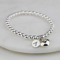 Silver beaded bracelet with a heart charm and round tag on a light gray background