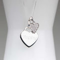 A silver heart pendant necklace with an engraved name and a smaller pavé heart charm, displayed on a white jewelry bust.