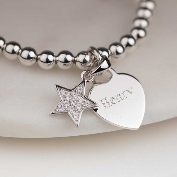 Silver beaded bracelet with star and heart charm on a light background