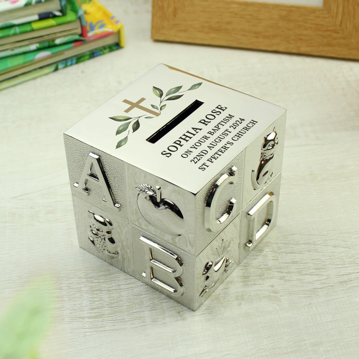 Decorative silver money box with engraved text on a light wooden surface