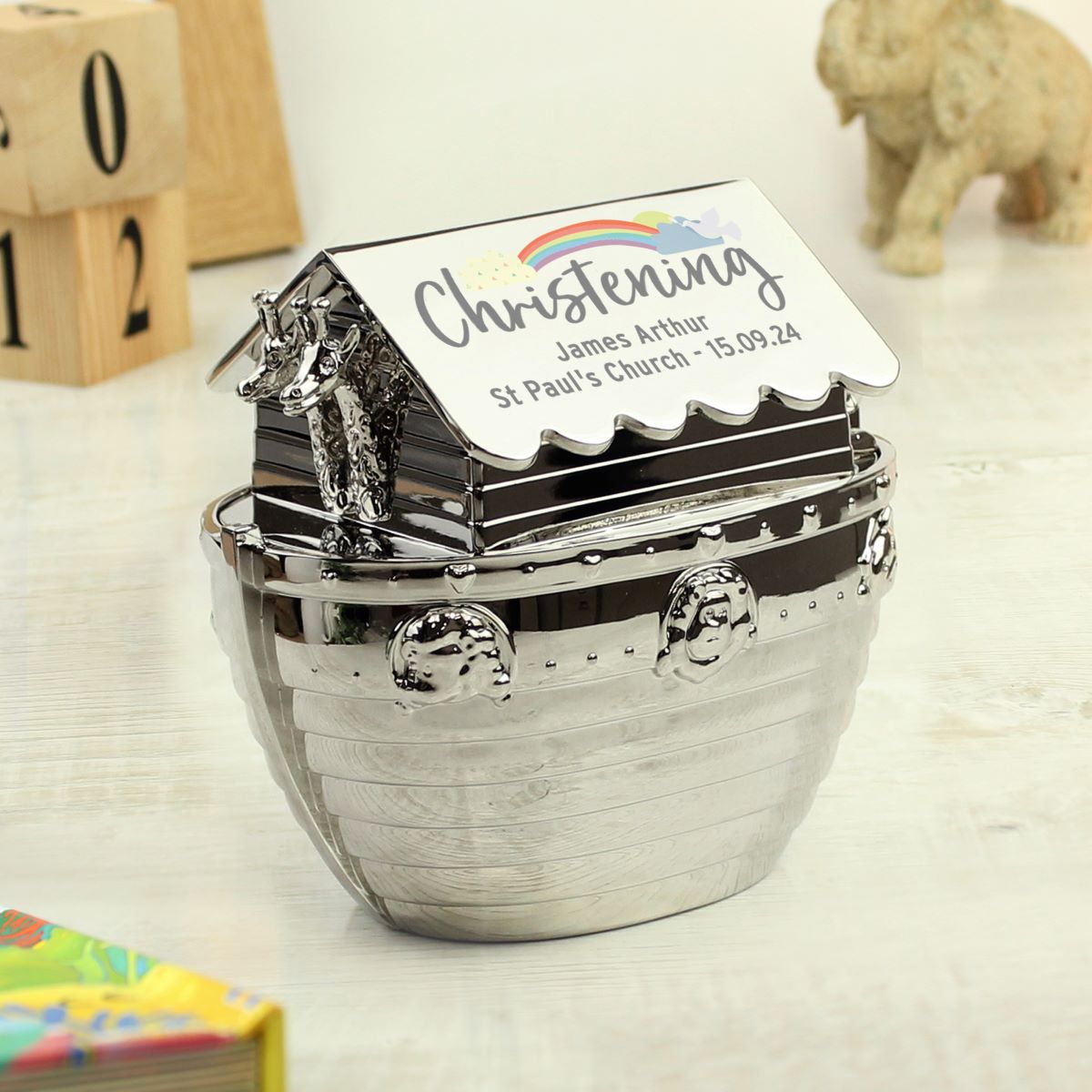 Decorative money box with 'Christening' text and rainbow design on a wooden surface.