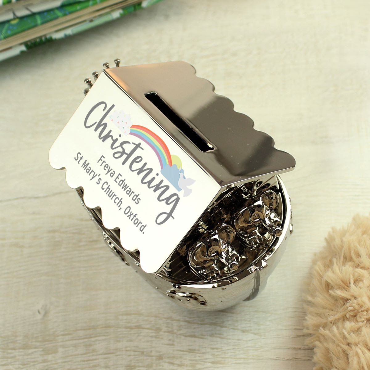 Decorative money box with 'Christening' text and rainbow design on a wooden surface.