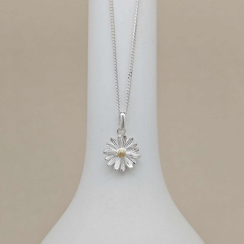 A silver daisy flower pendant necklace with a small gold center, displayed on a white jewelry bust against a beige background.