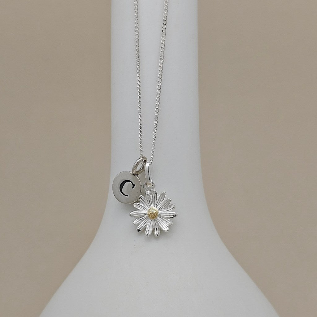 Silver necklace with a flower pendant and initial charm on a white stand.