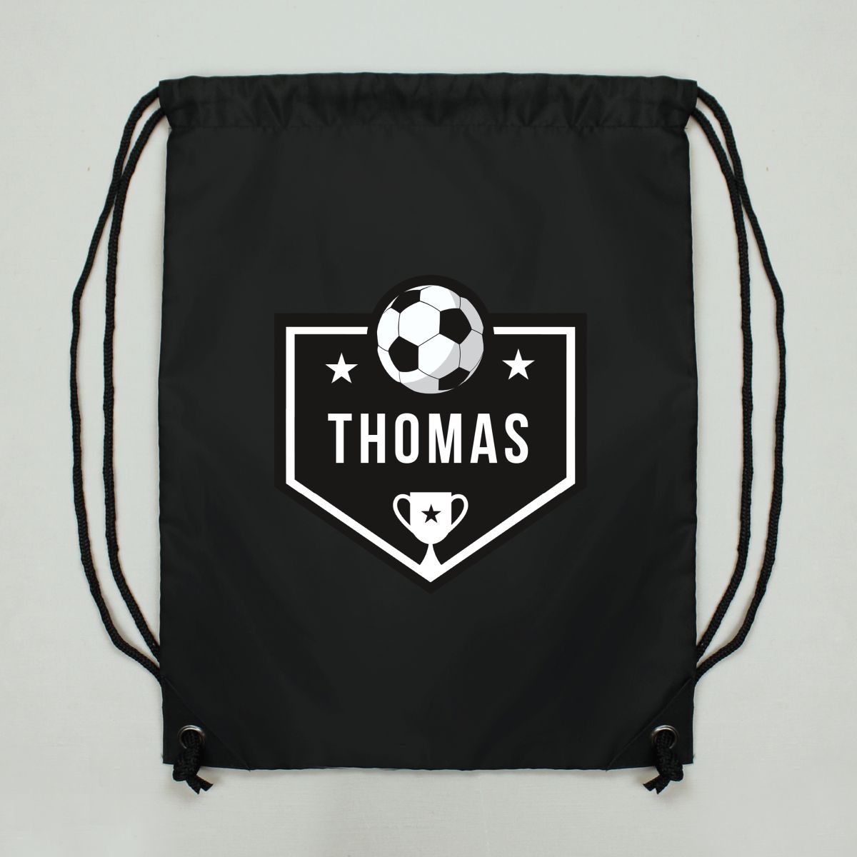 A black drawstring backpack with a white custom graphic on the front featuring a soccer ball, shield, stars, and the name 'THOMAS'.